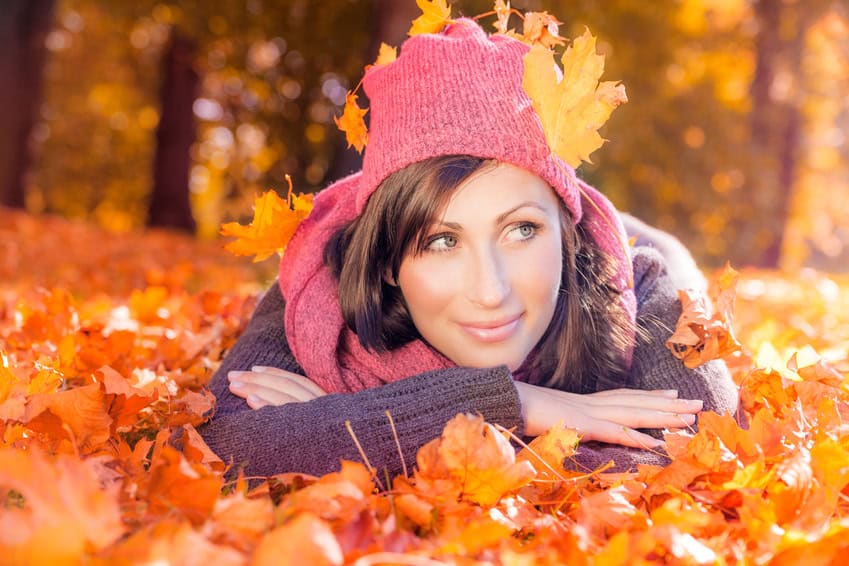 Frau im Herbstlaub mit pinker Mütze und gelben Blättern.